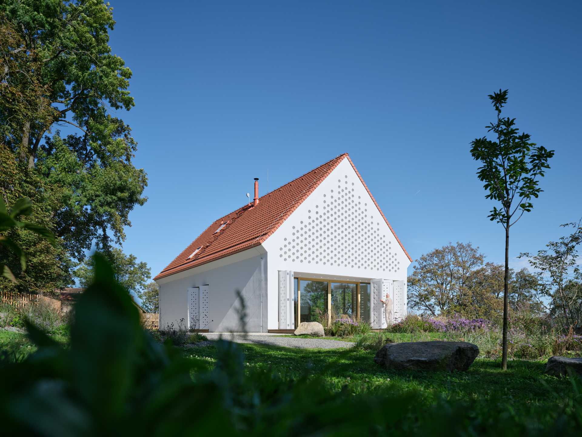 A modern home has perforated areas that act as a sunshade and a gabled roof.