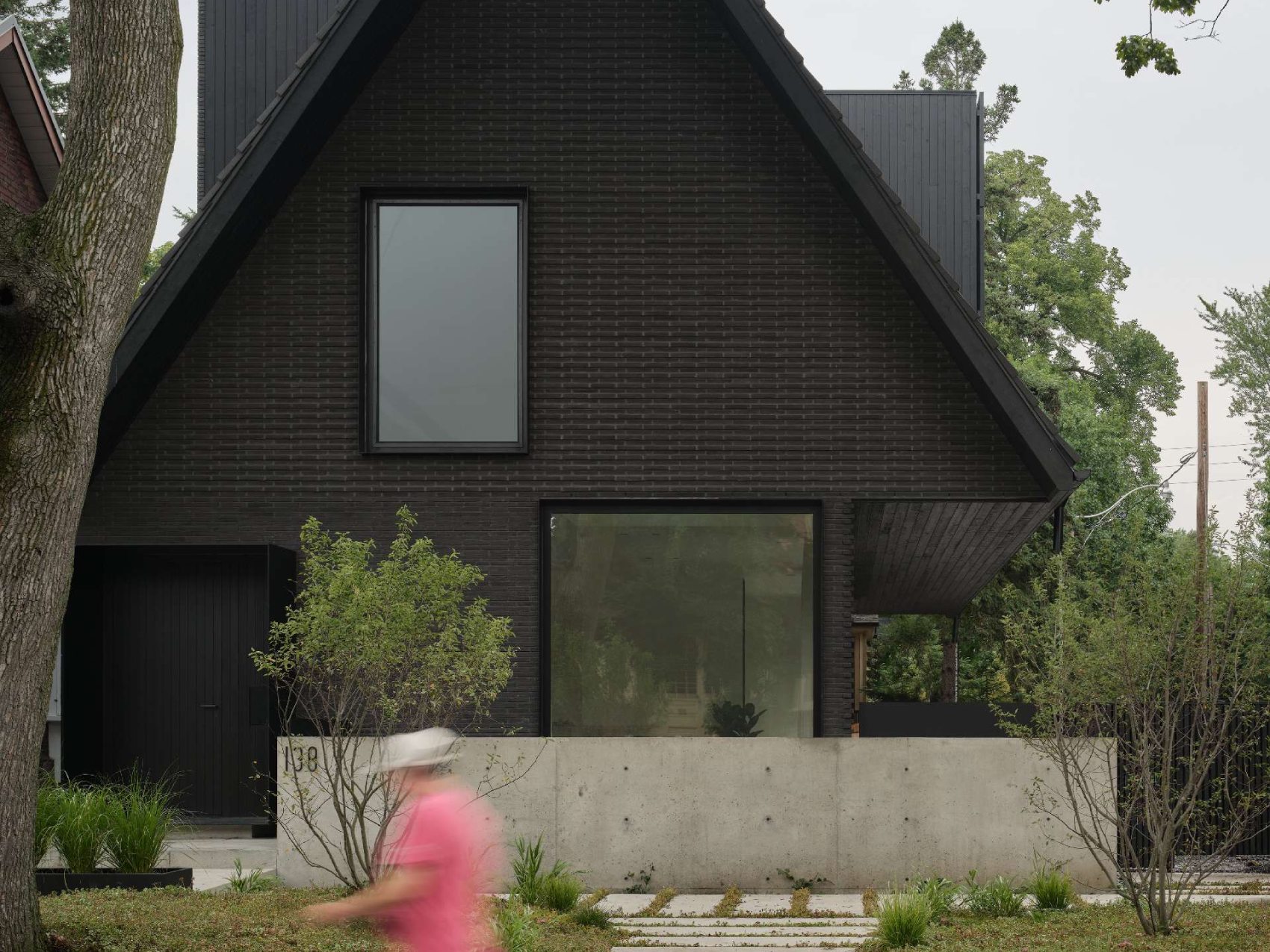 The palette of this modern home with a steep pitched roof, includes terracotta roof shingles, hand pressed brick, vertical hand brushed wood siding, powder-coated aluminum details, and raw galvanized steel.