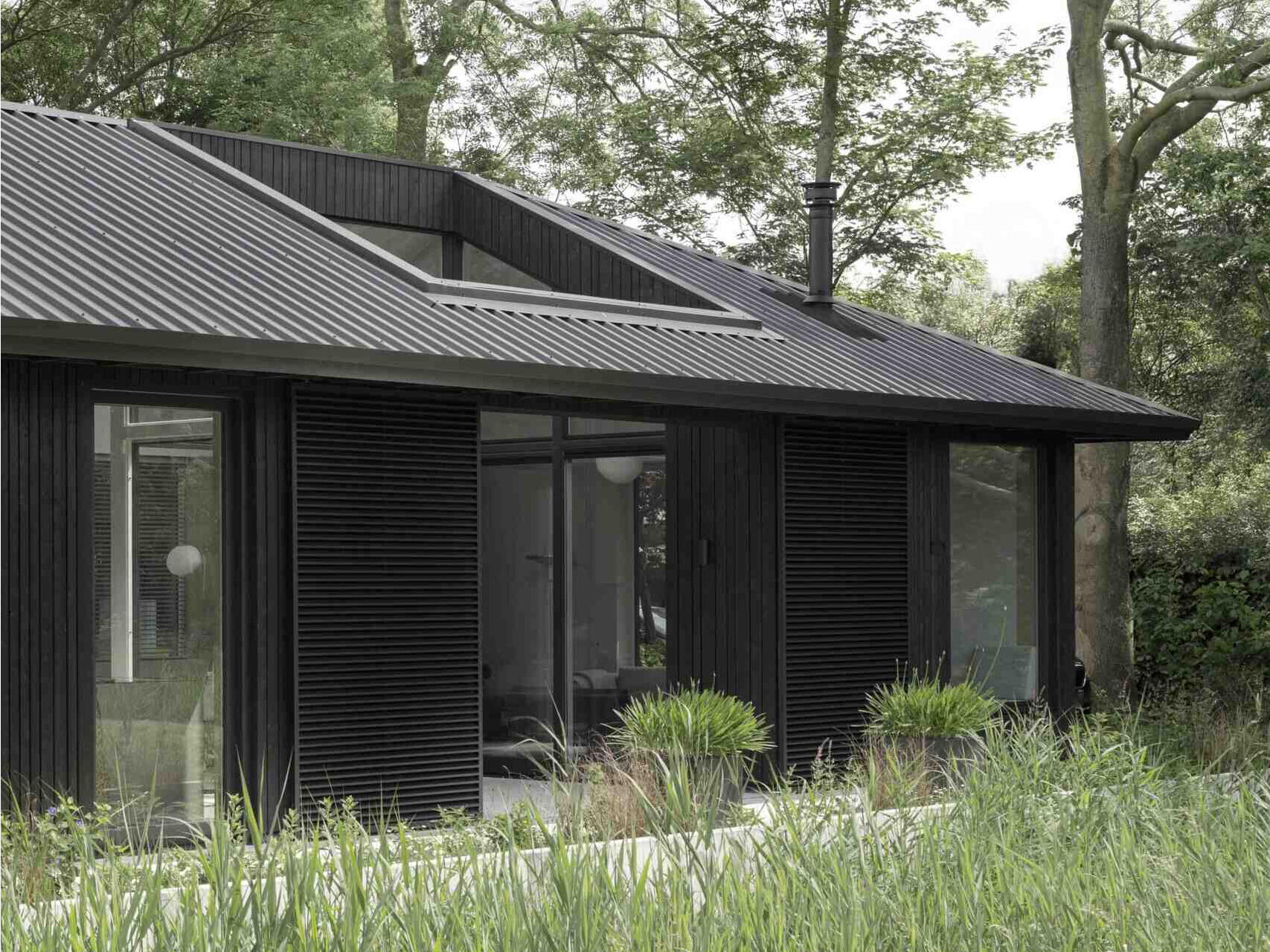 A modern and compact home with black waxed-wood cladding and extended rooflines.