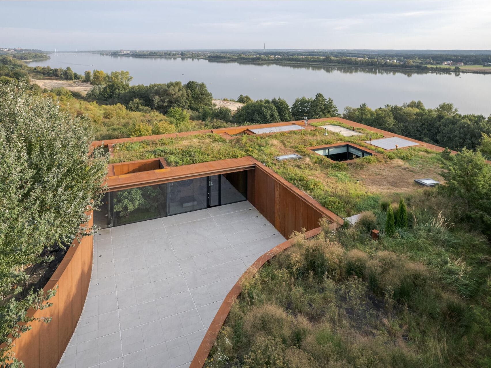This modern home vanishes into the hillside with a green roof, corten steel facade, and panoramic river views.