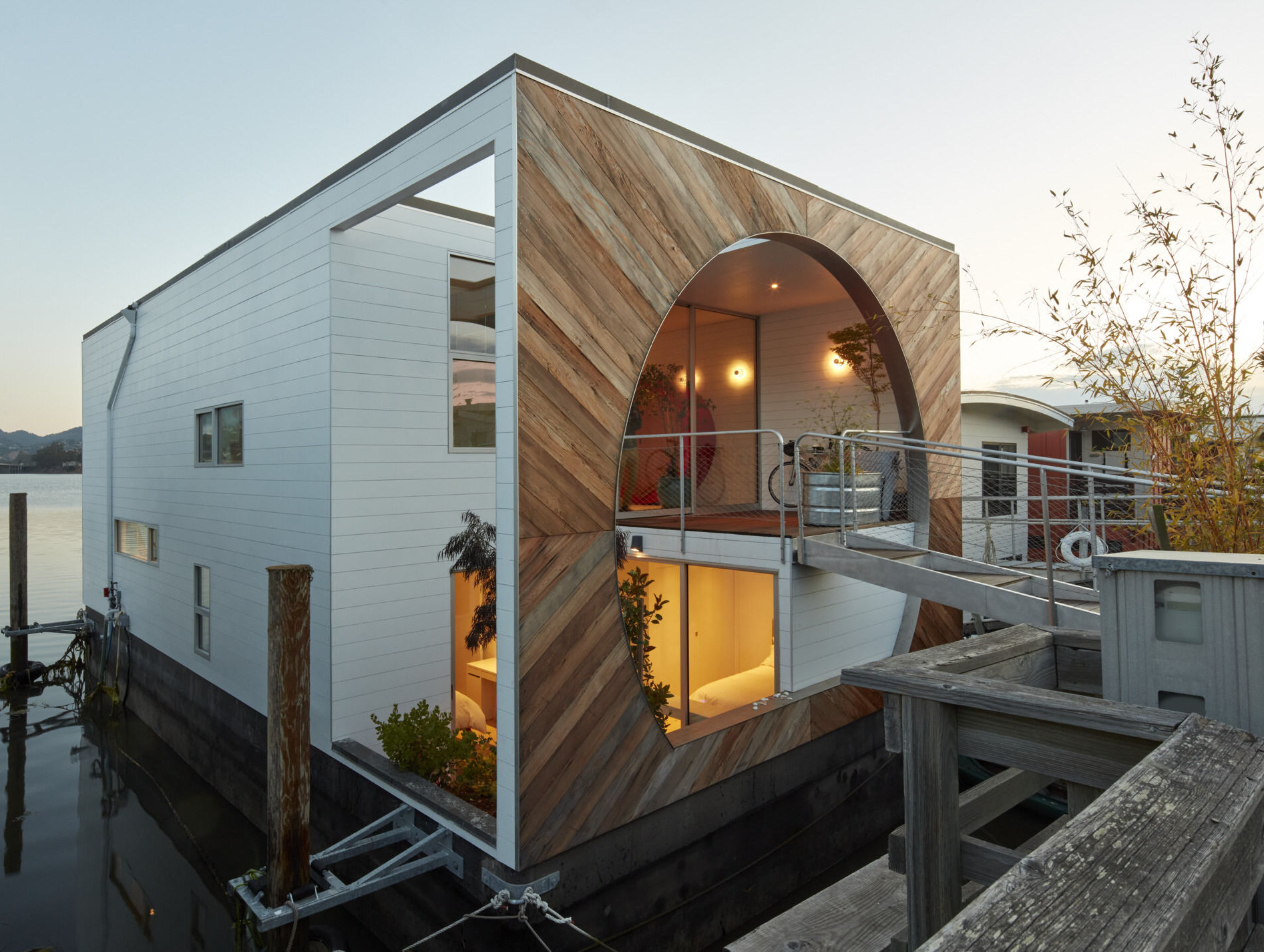 This modern houseboat showcases authentic waterfront living through its compact, efficient design. Featuring natural wood, weathered metal, and expansive glass, the layered structure blends seamlessly with its environment while honoring the community’s experimental roots.
