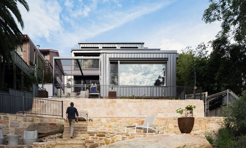 A contemporary home rises along a steep slope and blends seamlessly with the surrounding bushland. Built with fire-resistant materials and steel shutters for protection, the house balances safety with style, featuring multi-level living, expansive picture windows, and a strong connection between indoors and outdoors.