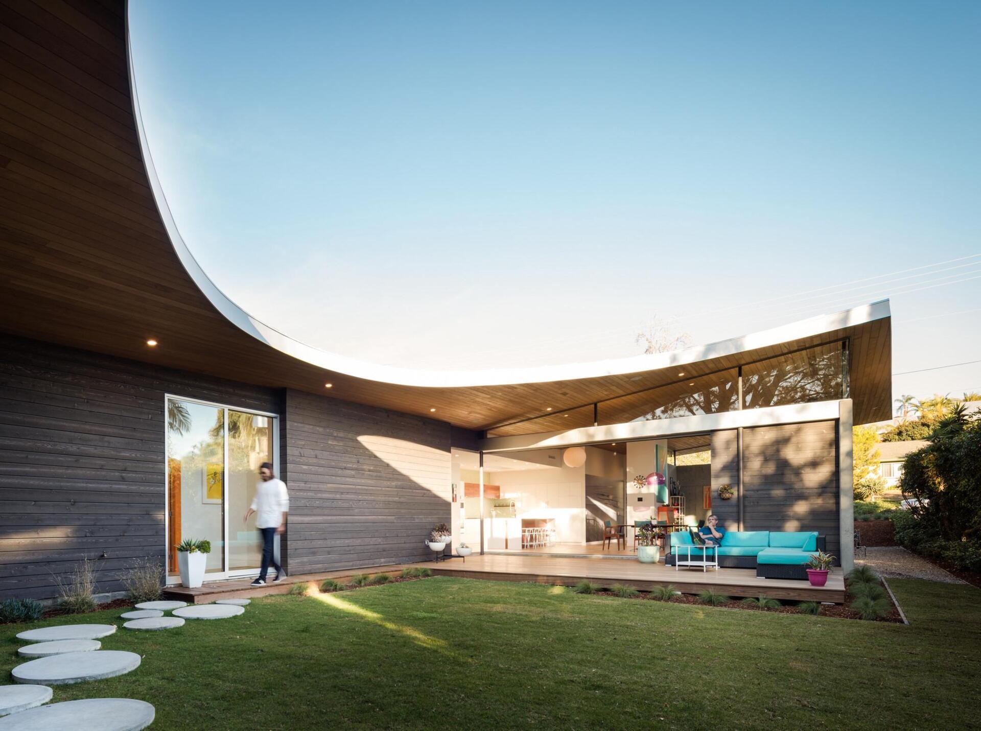A sweeping curved roof defines the architecture of Avocado Acres House, uniting three pavilions around a central courtyard. Influenced by mid-century modern design yet built with 21st-century sustainability, the home blends bold geometry, natural light, and playful details for a striking coastal residence.