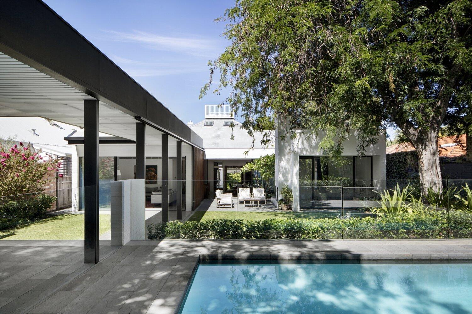 A refined modern house extension  with white brick volumes and dark steel and wood accents surrounded by lush gardens.