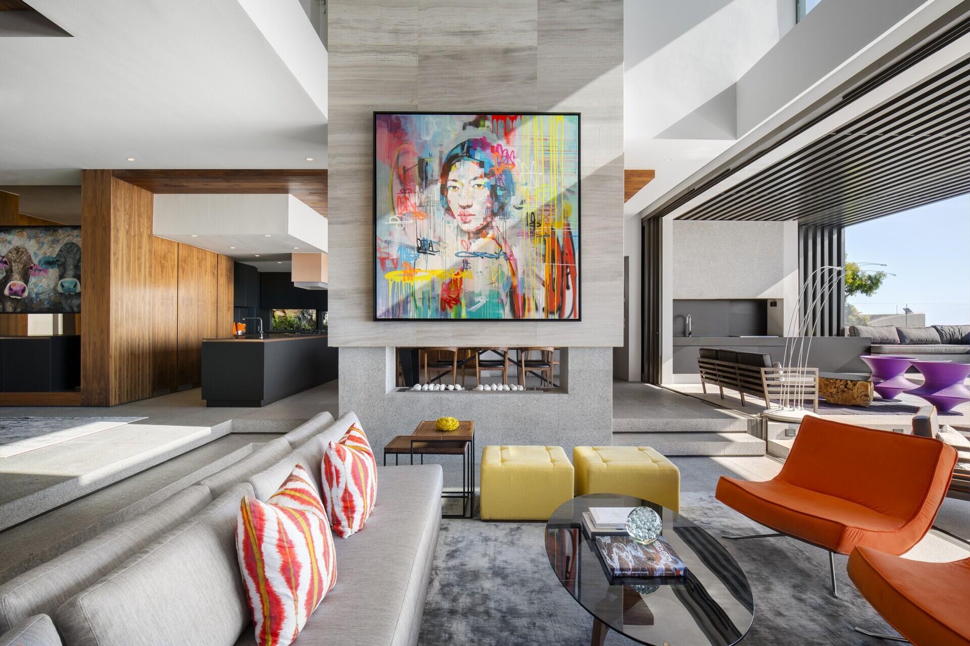 A vibrant, contemporary living room with a double-sided fireplace opens to a covered outdoor lounge and plunge pool.