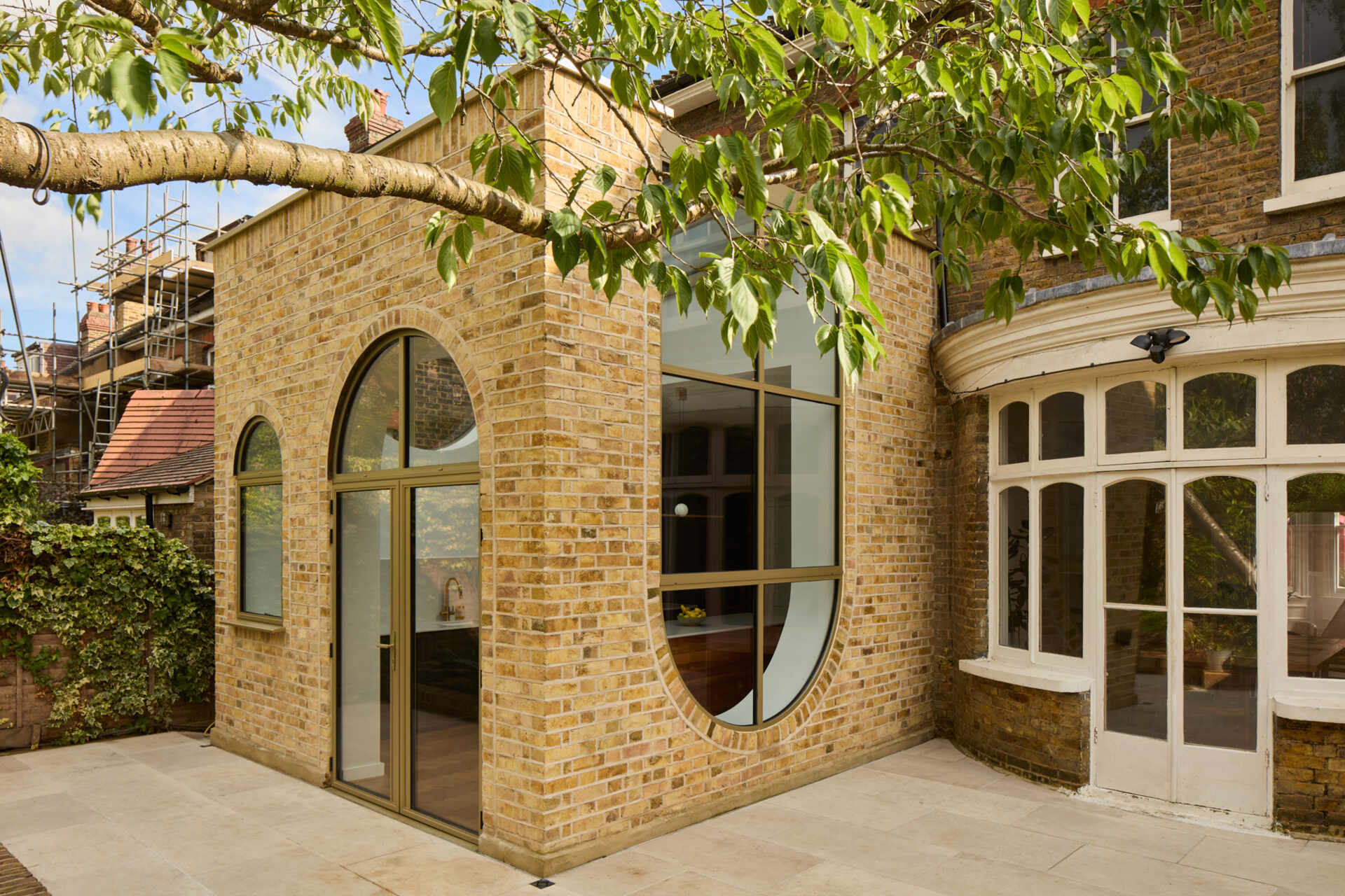 This rear extension of Perry Vale House reinterprets Edwardian craftsmanship with playful arches, reclaimed yellow London Stock Brick, and metallic bronze framing.