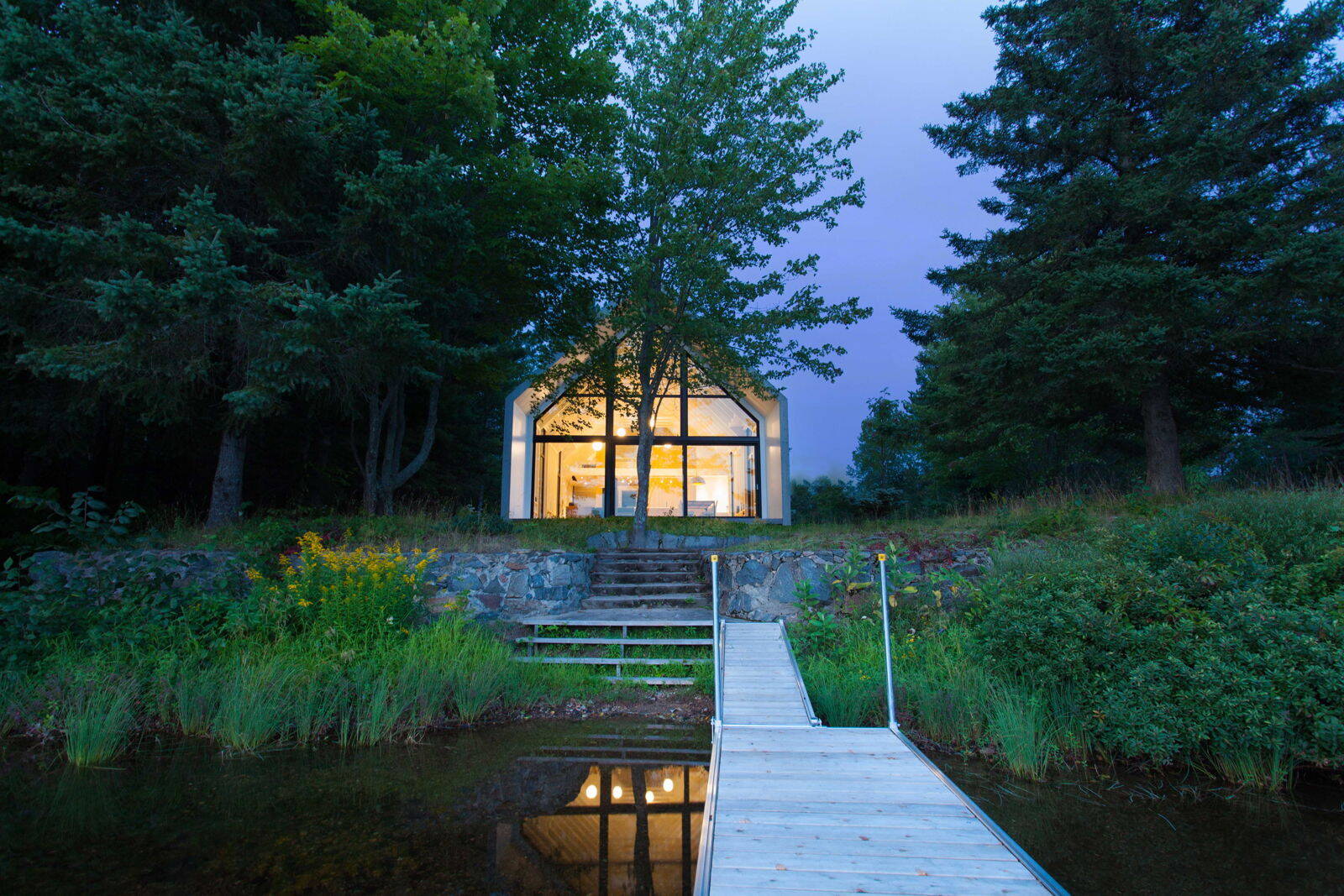 A calm cedar clad cottage in Quebec sits lightly in a forest clearing, offering a simple and peaceful approach to lakeside living.