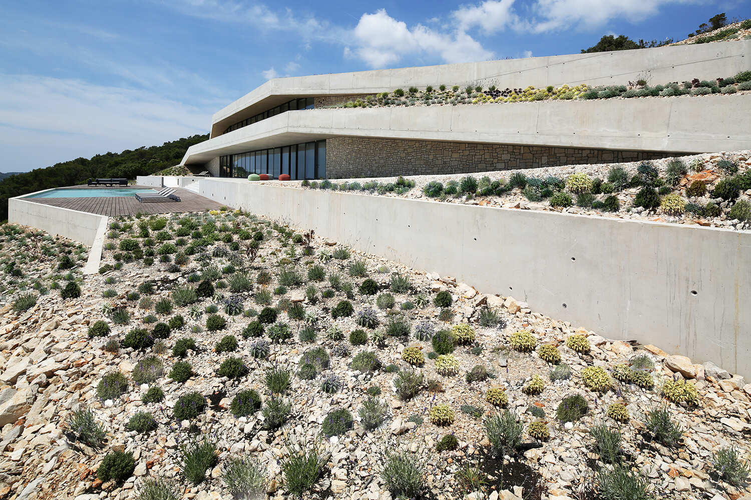 A modern concrete home built directly into a steep hillside on Vis Island, designed to sit within the landscape rather than on top of it.