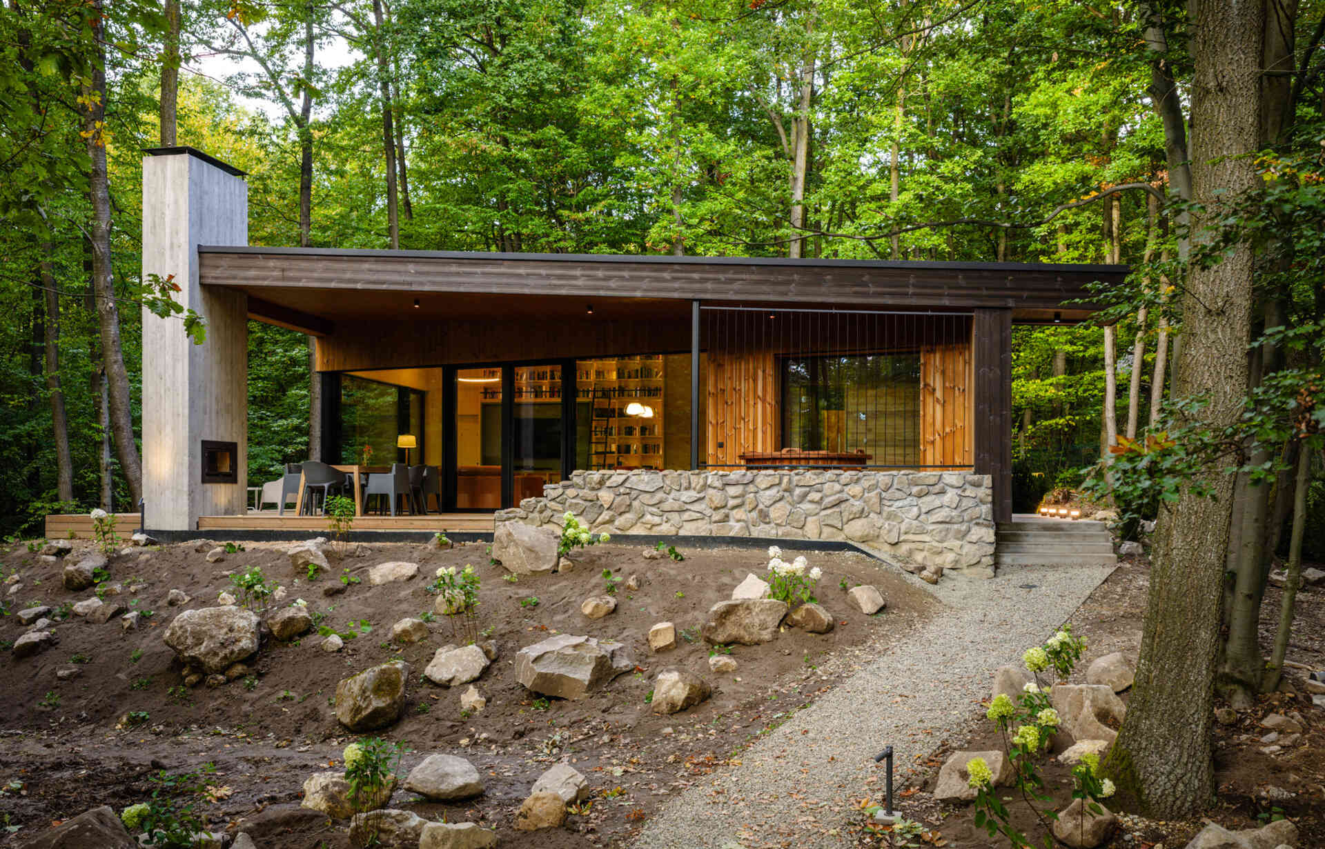 A modern forest home built from CLT and concrete, defined by a sculptural chimney and large glass openings.