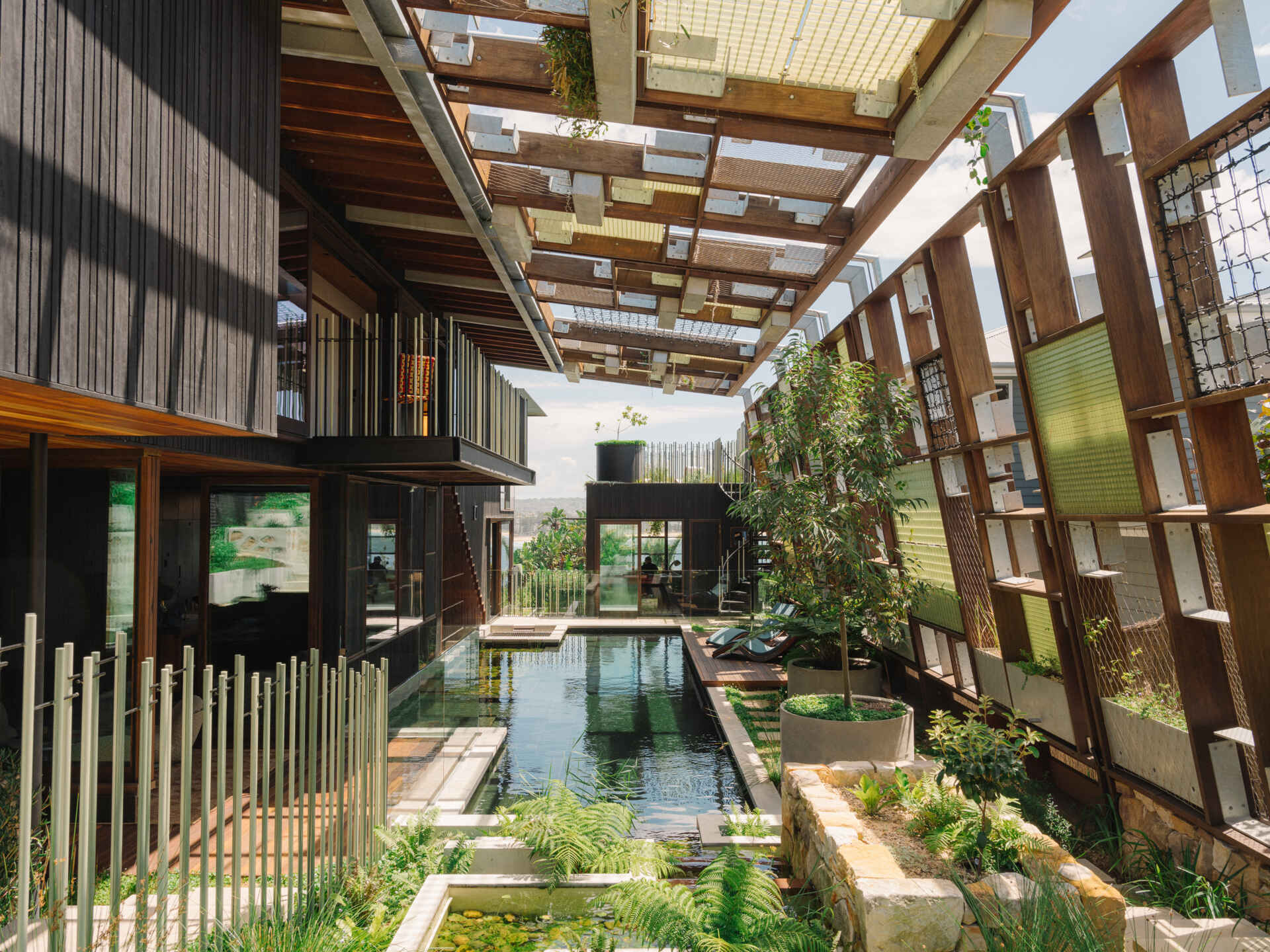 A natural swimming pool flows through the home beneath a canopy of plants and translucent FRP latticework.