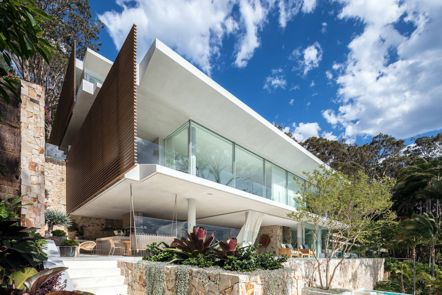 A terraced waterfront house steps down naturally on a steep slope with sandstone walls and a green roof.