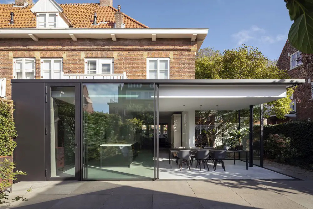 A minimalist glass extension contrasts beautifully with the brick architecture of a 1927 Dutch home, creating a light filled space that opens directly to the garden.