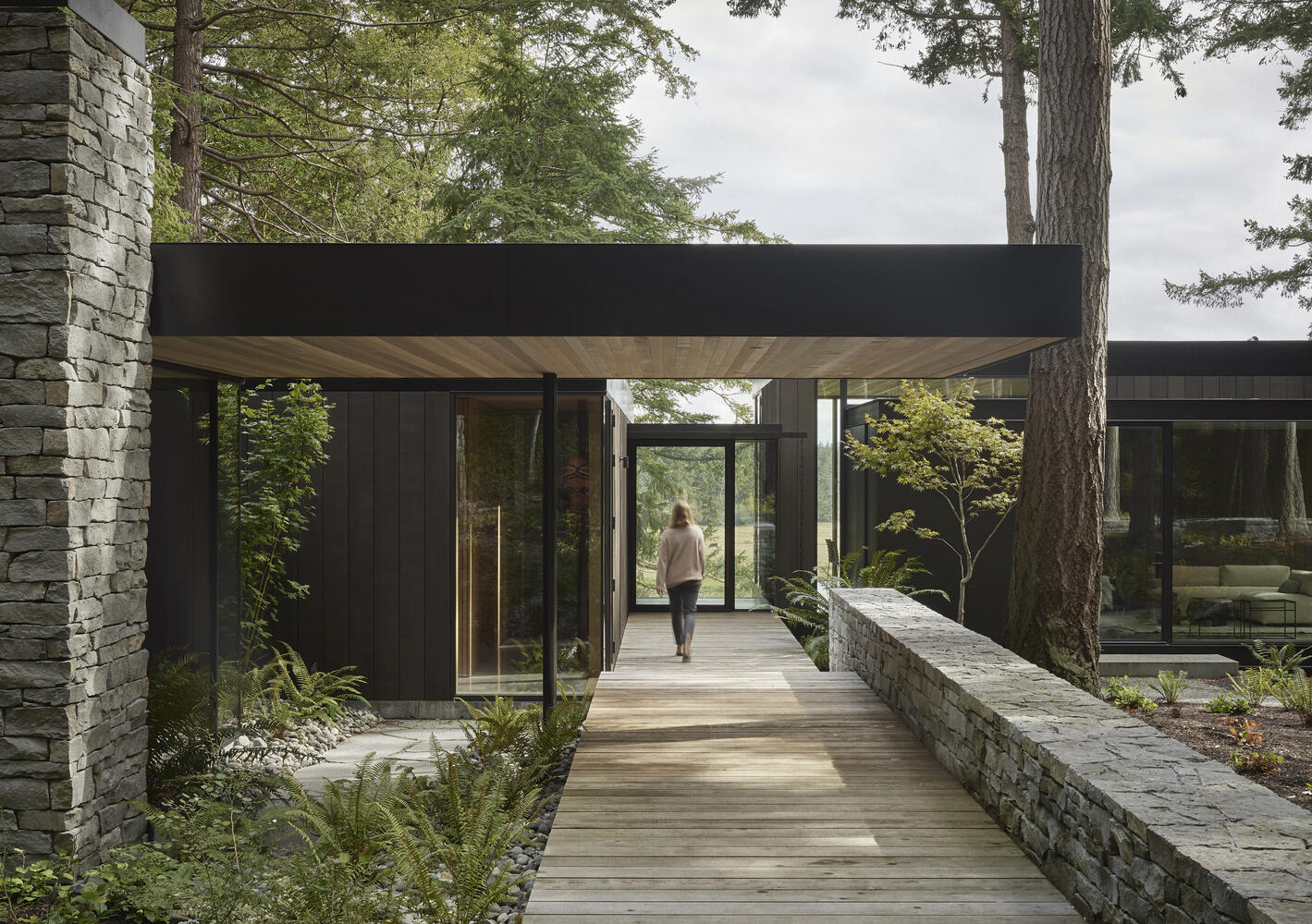 A modern farmhouse tucked into a forested hillside on Whidbey Island, overlooking barns, cattle fields and a pond. Warm wood and stone connect the home to its agricultural surroundings.