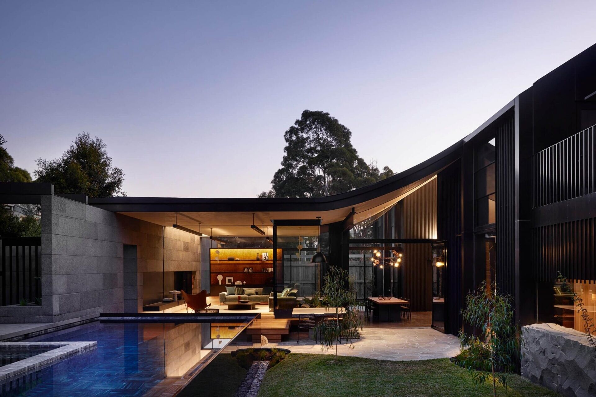 Sliding glass doors open to a timber deck, outdoor dining area, landscaped lawn and private swimming pool. The secluded garden setting balances the bold architecture.