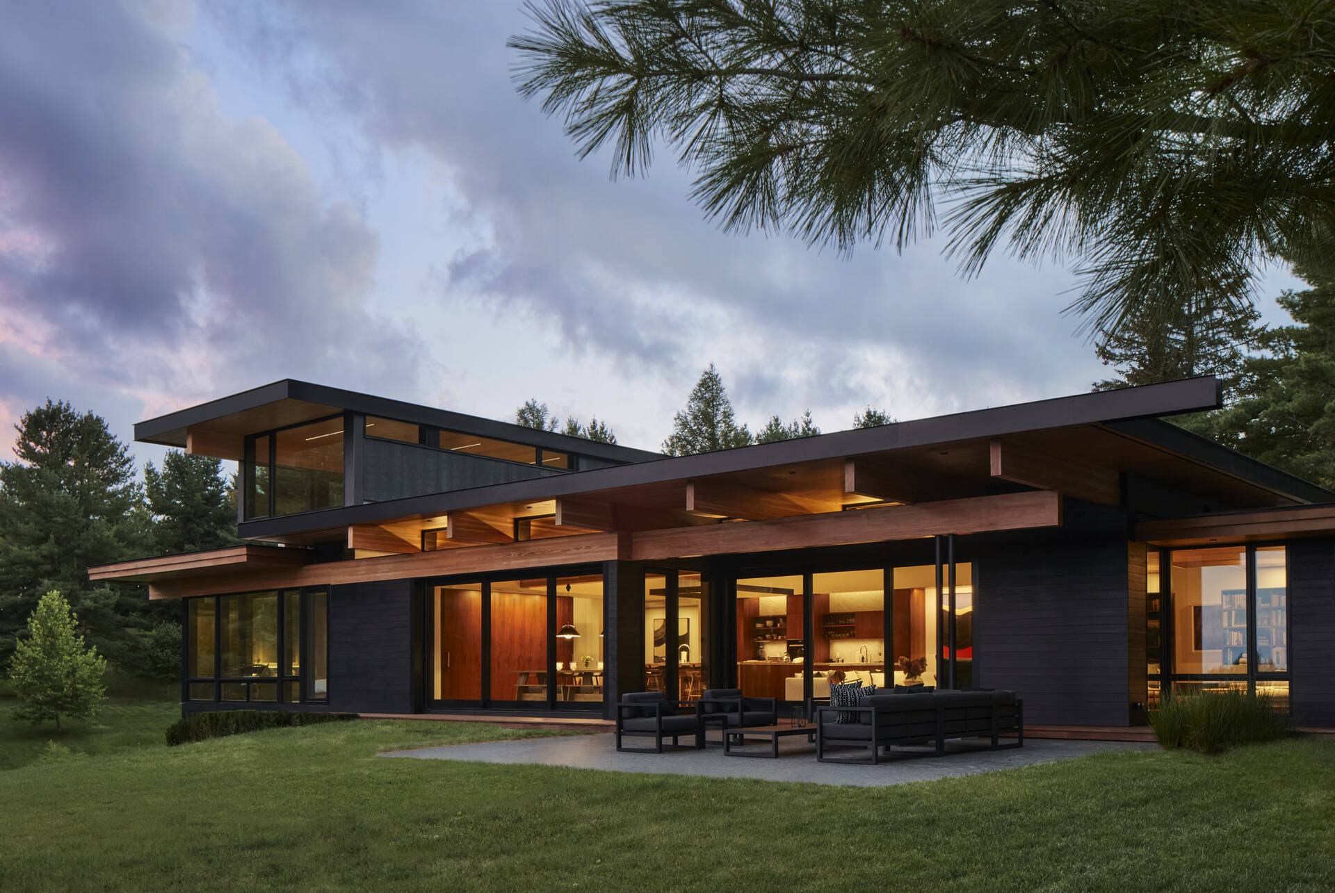 A low wall of stacked local granite organizes the home and references traditional field stone boundaries. Thermally modified ash cladding, locally sourced wood, concrete, stone, and blackened metal accents create a durable exterior rooted in place.
