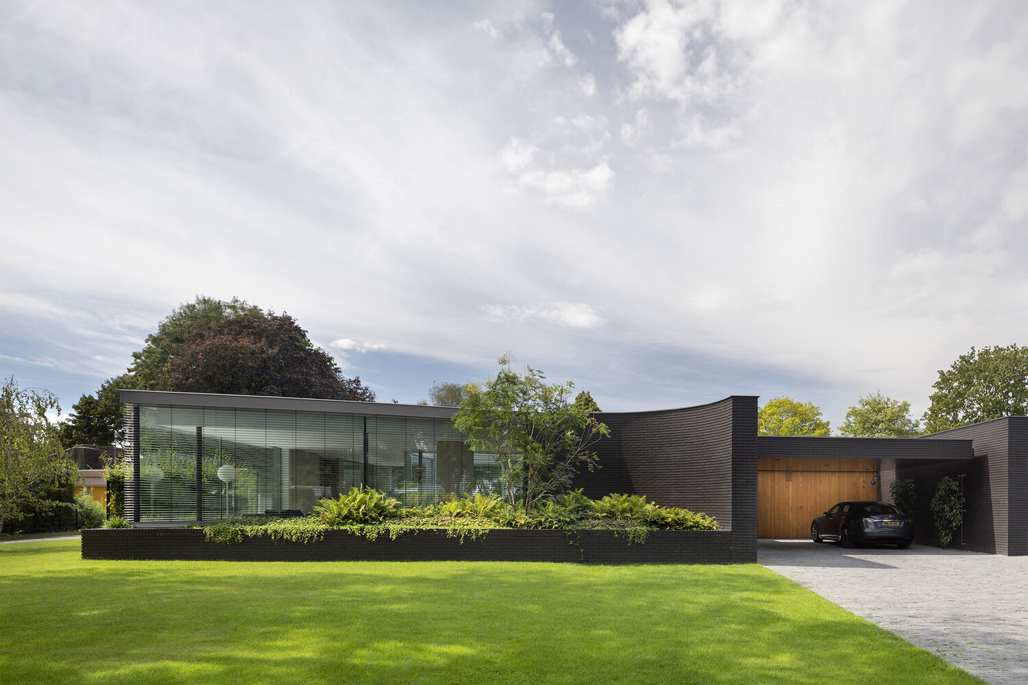 Curved black brick walls and built-in planters filled with greenery give this modern Dutch villa a bold yet natural presence.