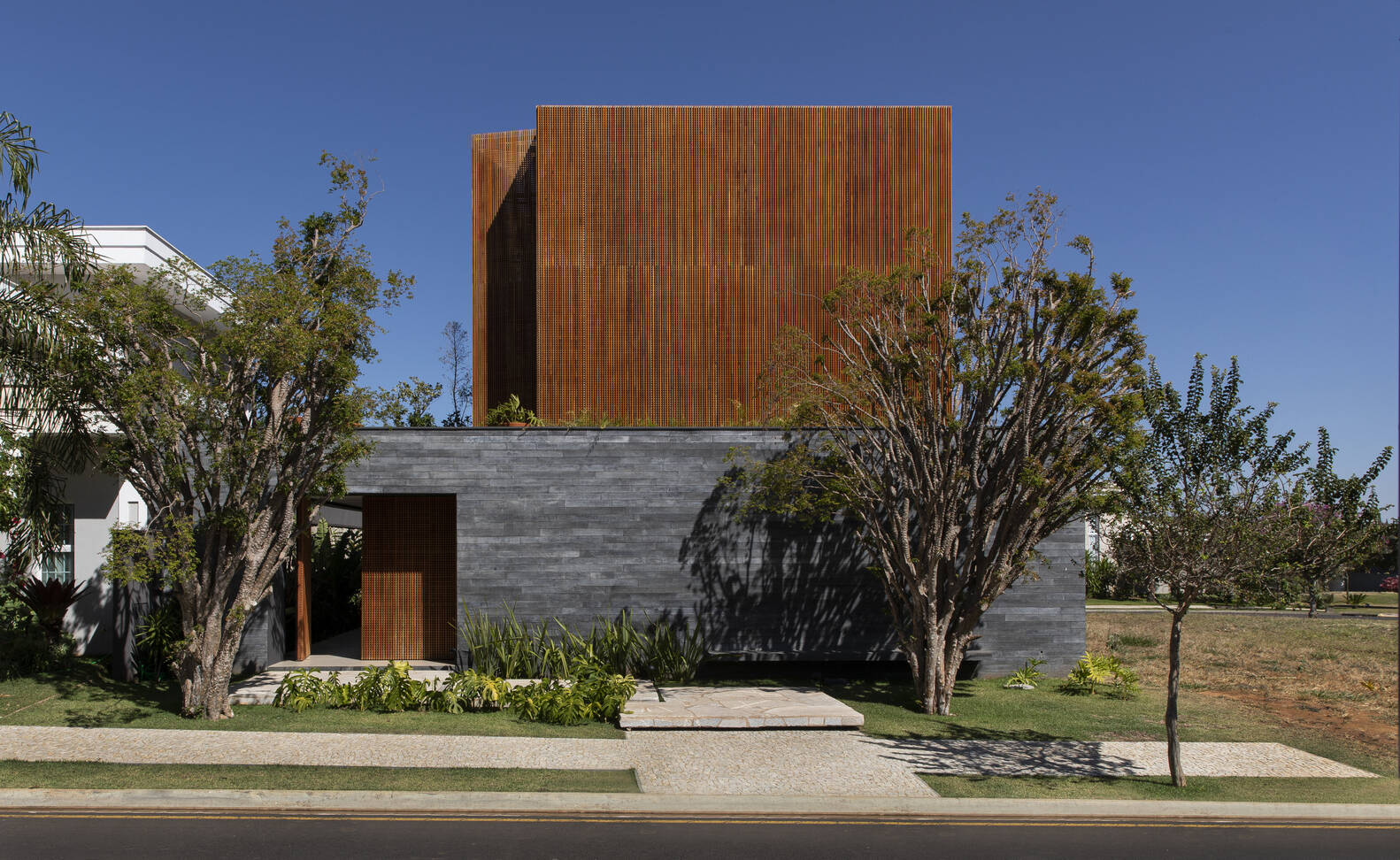 Discover a São Paulo home by mf+arquitetos where wood, black stone, and concrete create warmth, privacy, and modern elegance.