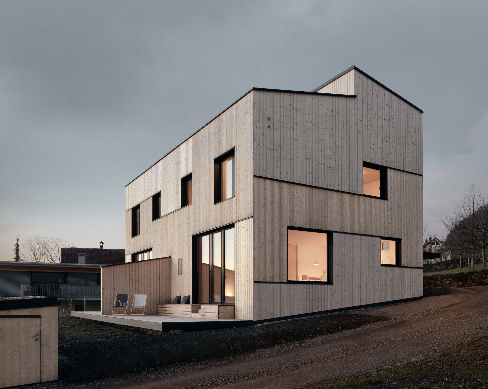 Light wood cladding in mixed widths creates a soft rhythm across this modern Austrian home, balanced by crisp black accents.