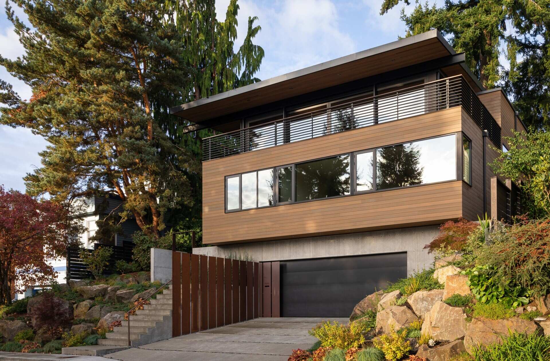 A modern Seattle facade with concrete, wood, and steel, softened by a garden approach and elevated entry sequence.